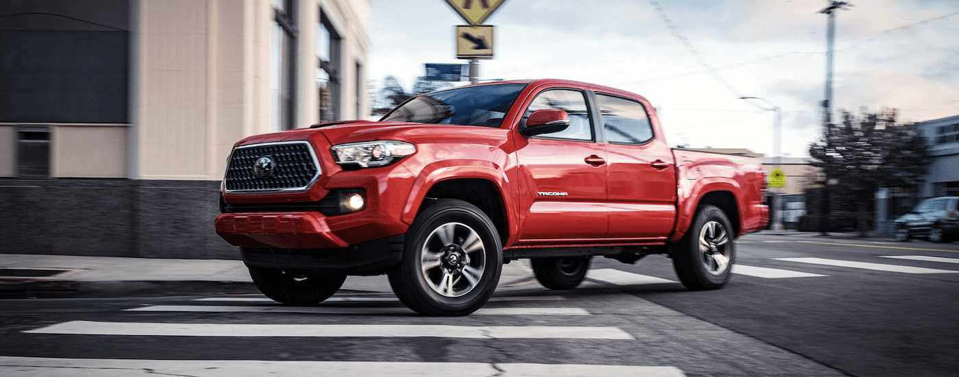 Orange 2018 Toyota Tacoma driving safely down a city street