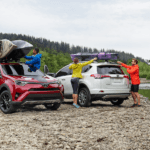 Red and white 2019 Toyota Rav4s with canoes next to river