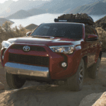 Red 2019 Toyota 4Runner with luggage on top climbing mountain with lake and mountains in background