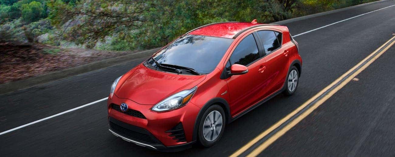 A red 2019 Toyota Prius C travel a wet rural road