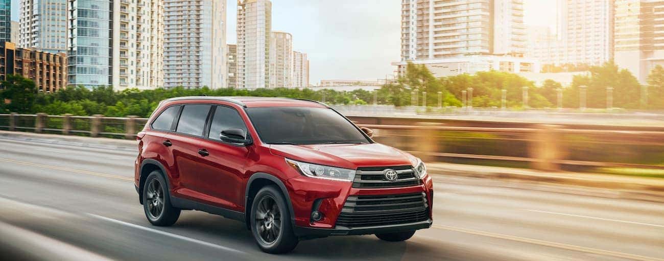 A red 2019 Toyota Highlander drives away from a city at sunset