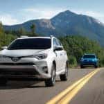 A white and blue Toyota RAV4 on an empty mountain road