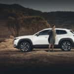 Man putting on a jacket standing outside of a Mazda CX-50 hybrid