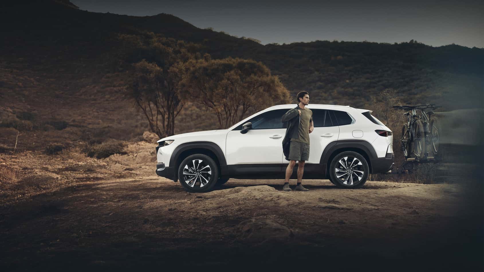 Man putting on a jacket standing outside of a Mazda CX-50 hybrid