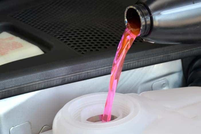 stainless steel container pouring pink liquid into a white/clear container