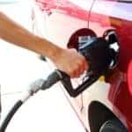 Close up image of a man pumping gas into a red car.