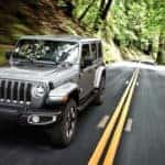 Image of a silver 2019 Jeep Wrangler driving on a forest highway.