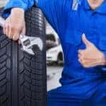 Image of a mechanic with a tire, holding a wrench, and giving a thumbs up.