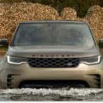 Front view of a bronze 2026 Discovery wading through a stream.