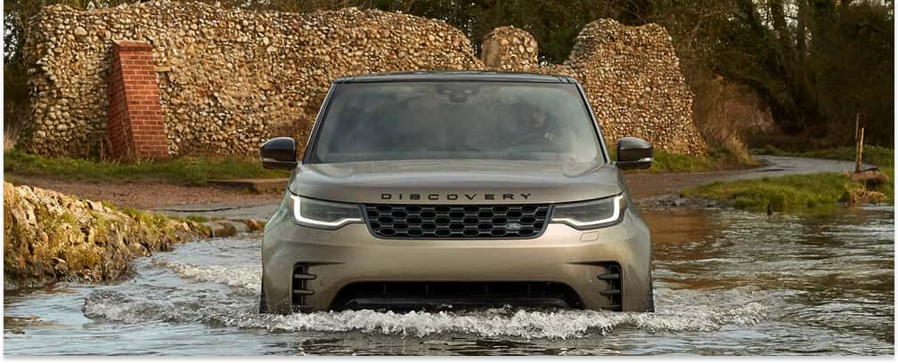 Front view of a bronze 2026 Discovery wading through a stream.