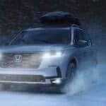 A silver Honda Pilot driving through the snow at night.