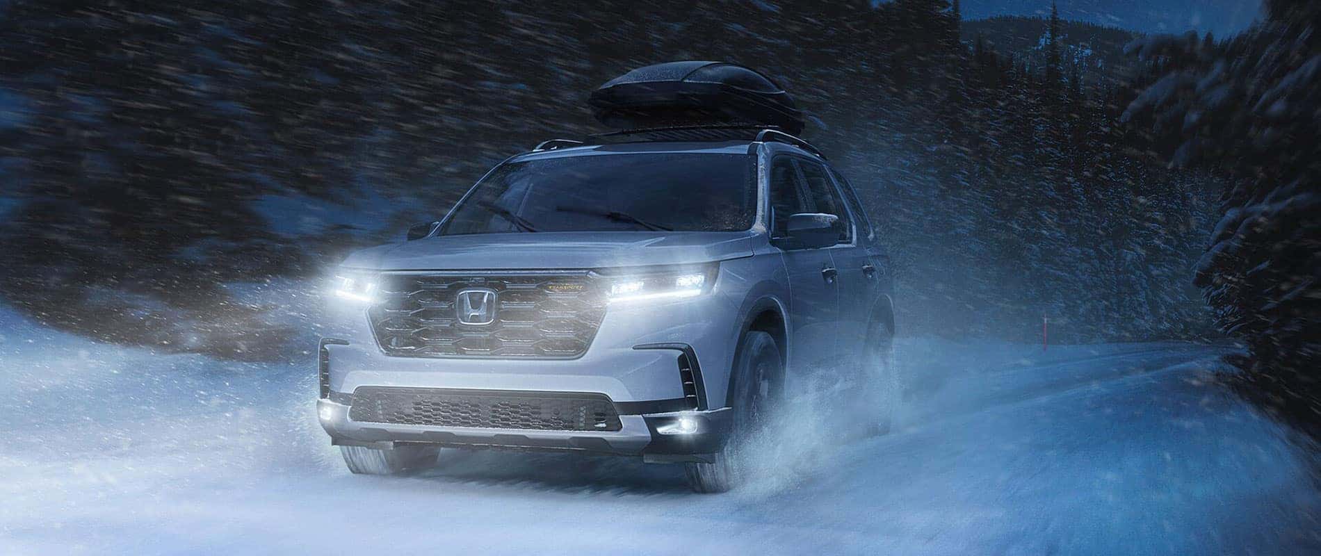 A silver Honda Pilot driving through the snow at night.