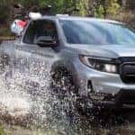 A silver Honda Ridgeline driving through mud while hauling a pair of dirt bikes.