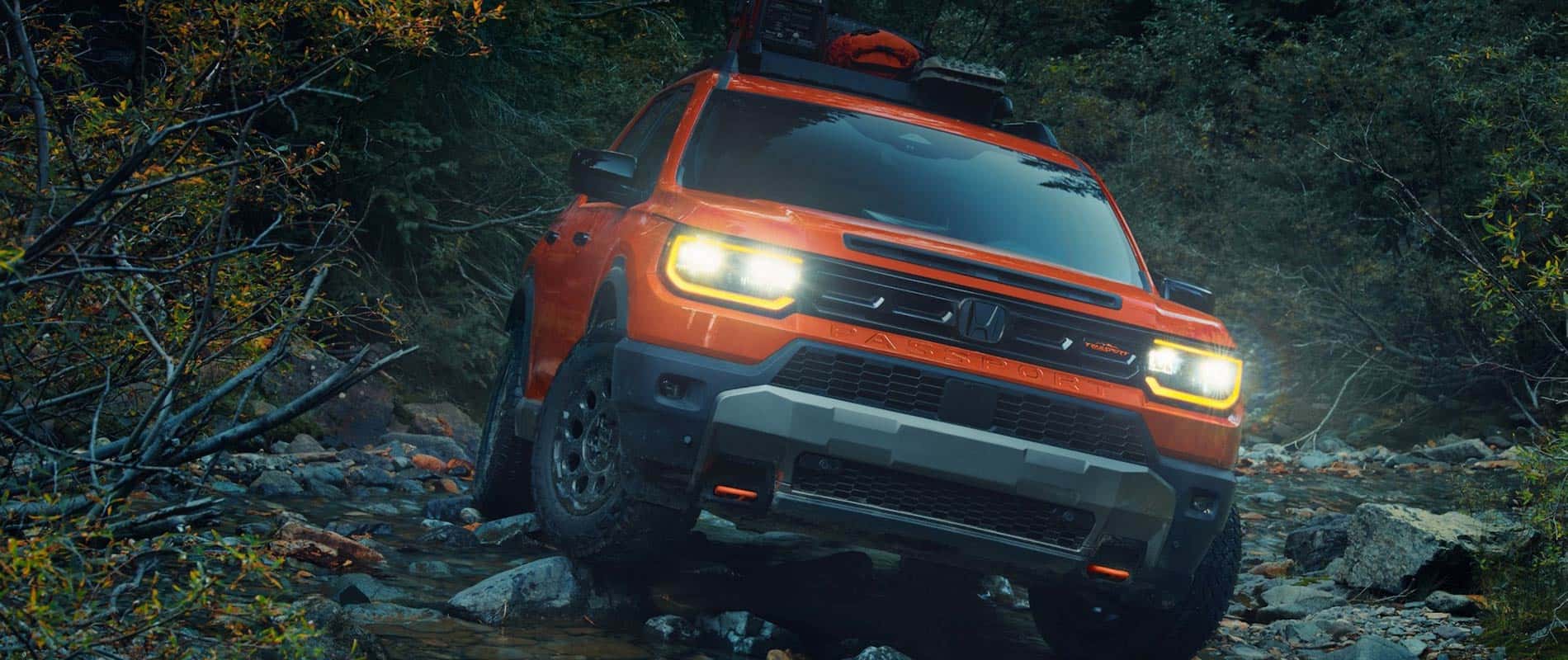 Used Honda Passport For Sale Near Jackson An front view of an orange Honda Passport driving over a creek with its headlights on.