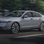 A gray Honda Accord Hybrid driving quickly down the street.