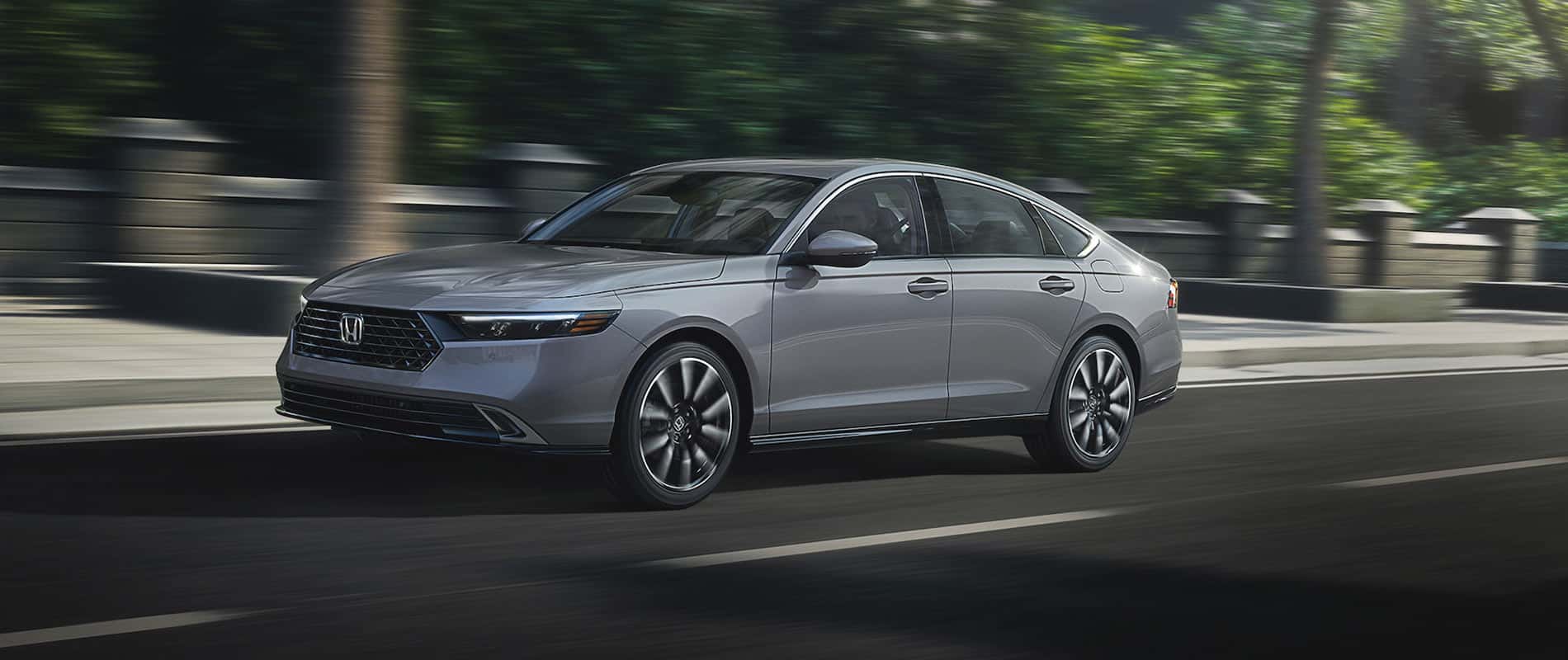 A gray Honda Accord Hybrid driving quickly down the street.