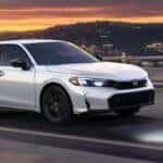 A silver Honda Civic Is driving over a bridge outside a city.