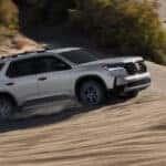 A silver Honda Pilot driving over sand dunes in a desert.