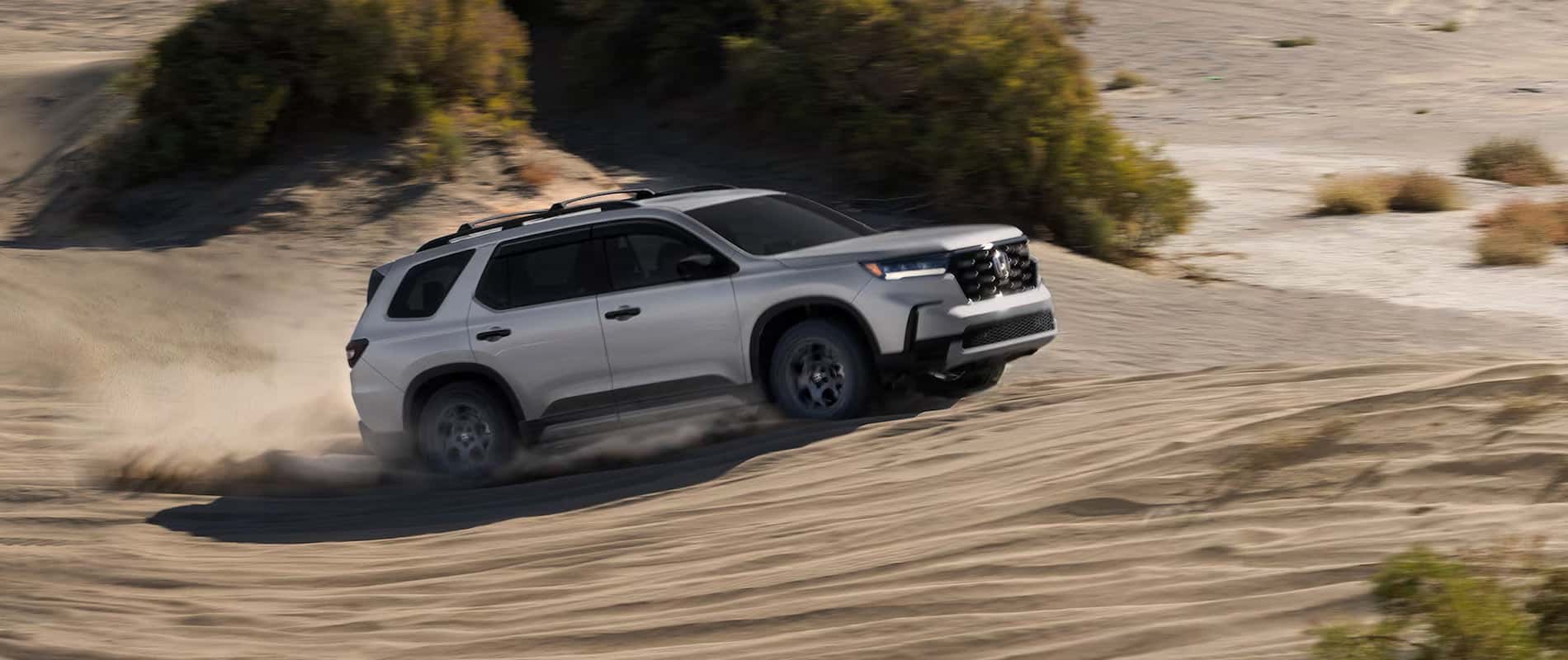 A silver Honda Pilot driving over sand dunes in a desert.