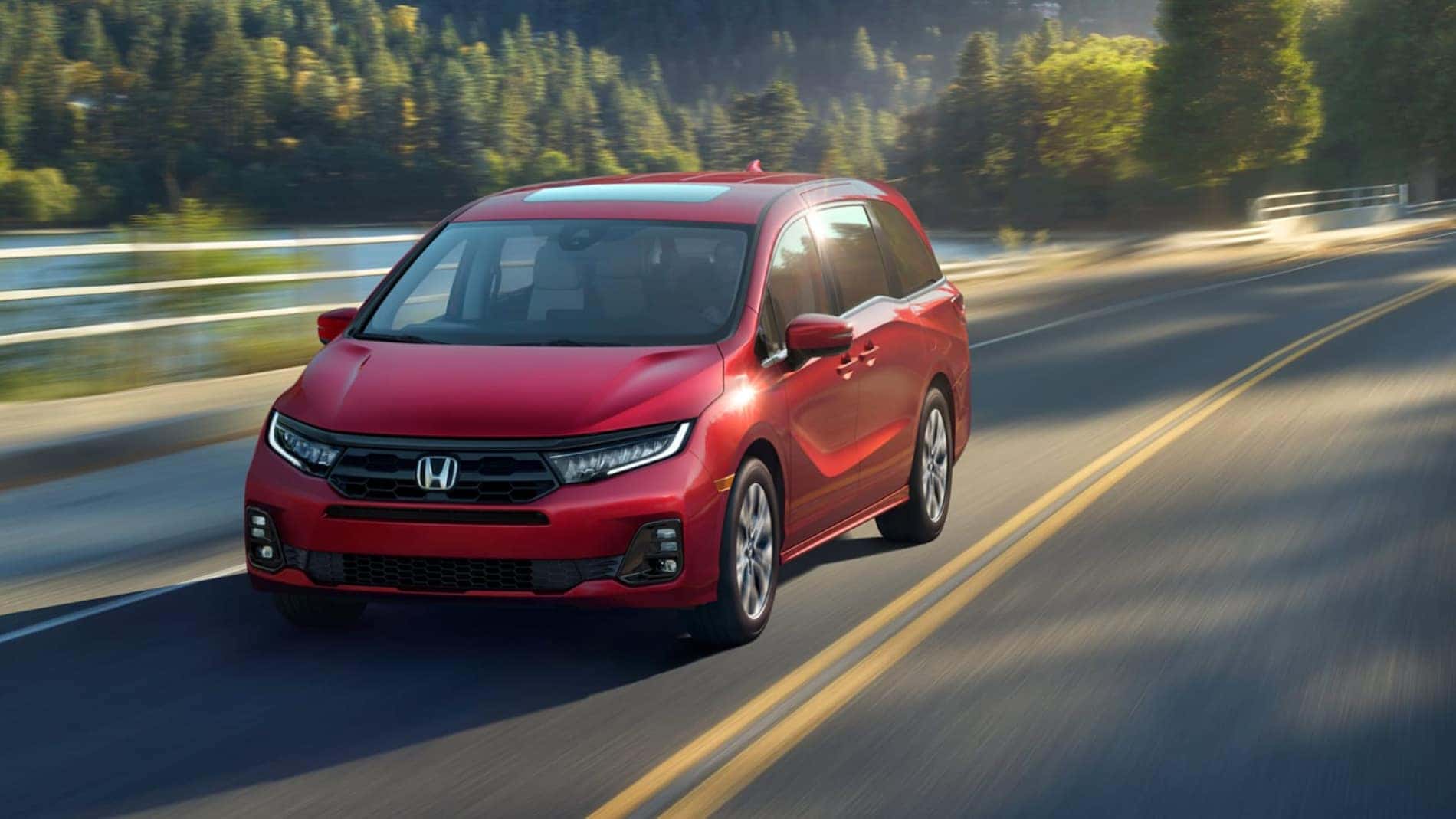 A red Honda Odyssey driving down a road by a lake.
