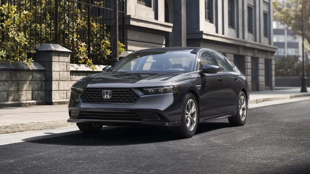 A dark grey Honda Accord parked by a curb in a city.