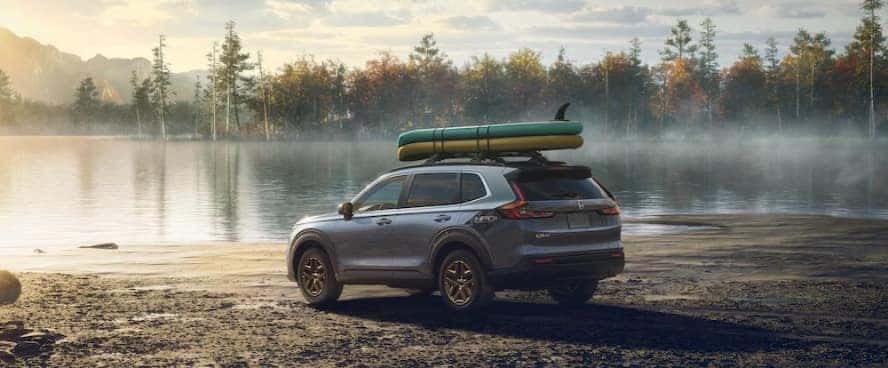 A gray 2026 Honda CR-V with boats on its roof rack, parked beside a lake