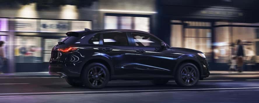 A dark blue 2027 Honda HR-V crossover SUV driving down a city street at night