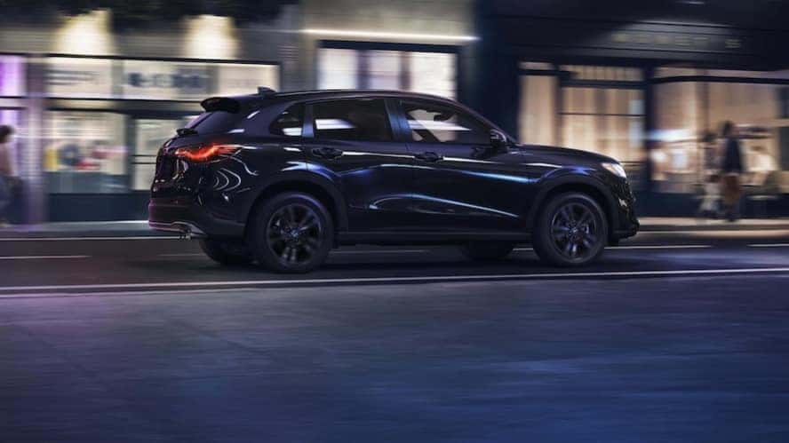 A dark blue 2027 Honda HR-V crossover SUV driving down a city street at night