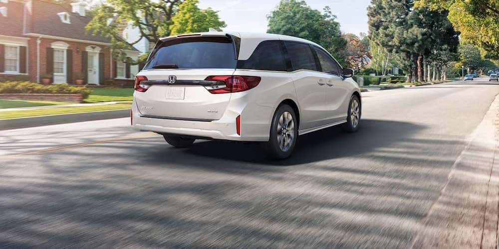 A white 2027 Honda Odyssey minivan driving down a suburban street