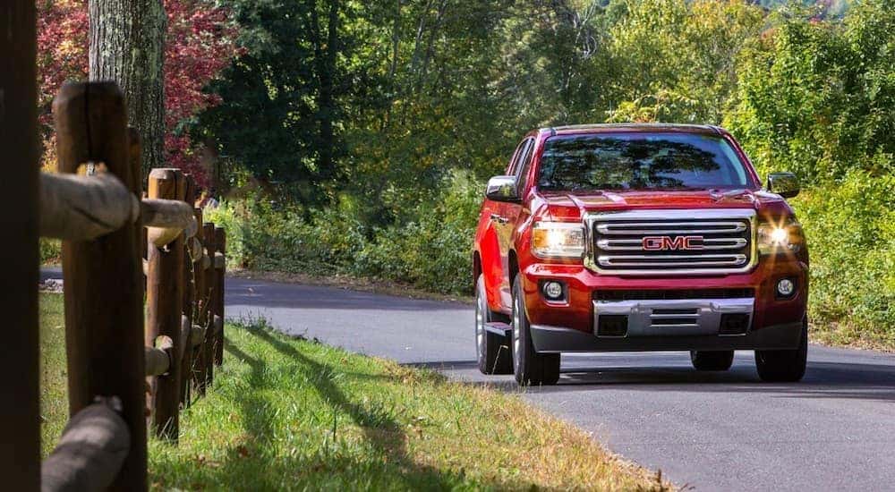 Red 2019 GMC Canyon driving down road with split log fence
