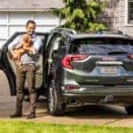 A man unloads a dog from a gray 2019 GMC Terrain Denali in a driveway