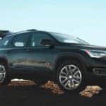 A man is lifting the tailgate of his black 2019 GMC Acadia. It is part of the GMC SUVs lineup.