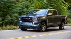 A grey 2017 GMC Sierra 1500, a popular choice for used trucks, is driving in front of trees outside Atlanta, GA.