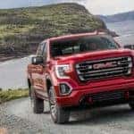 After leaving an Atlanta GMC dealer, a 2019 GMC Sierra 1500 AT4 is shown driving on a dirt road hill with a lake and mountains in the background.