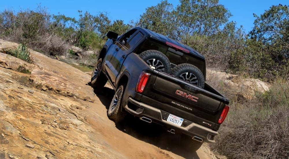 A black 2019 GMC Sierra is climbing a hill on a trail with spare tires in the bed.