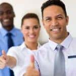 Three sales assistants are at a used car dealer near Atlanta, GA with their thumbs up and smiling.