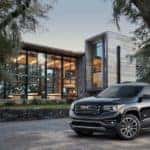 A black 2017 GMC Acadia is parked in front of a building with trees around it. By searching 'used car dealership near me', you could find this vehicle.