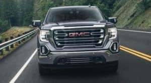 A black 2021 GMC Sierra 1500 is shown from the front on a road with pine trees.