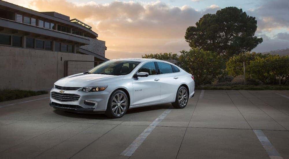 A white 2016 Chevy Malibu, a favorite among used cars for sale near Atlanta, GA, is parked in front of a house during a sunset.