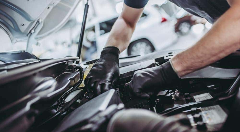 A mechanic with black gloves is working under the hood of a car.