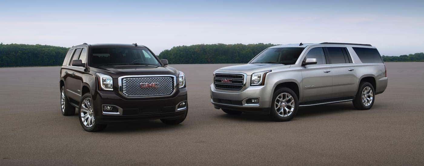 A black 2015 GMC Yukon and a silver XL are parked in an open parking lot.