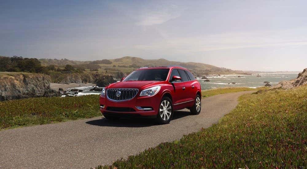 A red 2017 Buick Enclave is driving with the ocean behind it.
