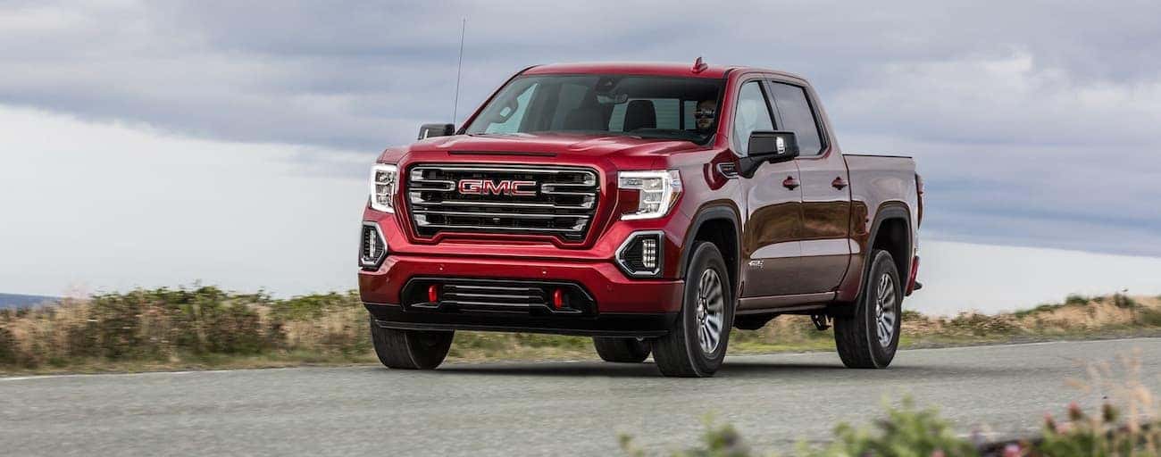 A red 2020 GMC Sierra 1500 AT4 is driving with clouds in the sky.