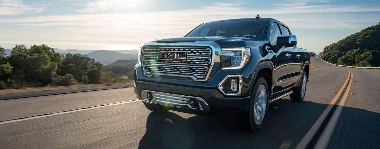 A black 2020 GMC Sierra 1500 Denali is driving with mountains in the distance.