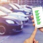 A man is holding up a phone with a list on it in front of a row os used cars for sale near Atlanta, GA..