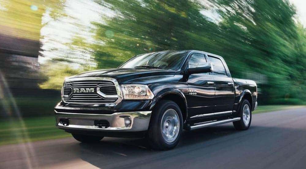 A black 2018 Ram 1500 is driving on a treelined road.