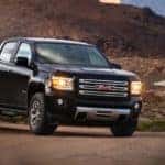 A black 2017 GMC Canyon is parked on a dirt path with mountains in the distance.