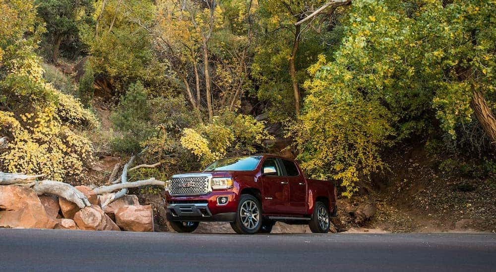 A red 2018 GMC Canyon, which is a popular option for used trucks for sale in Atlanta, GA, is parked next to large rocks and tall trees.