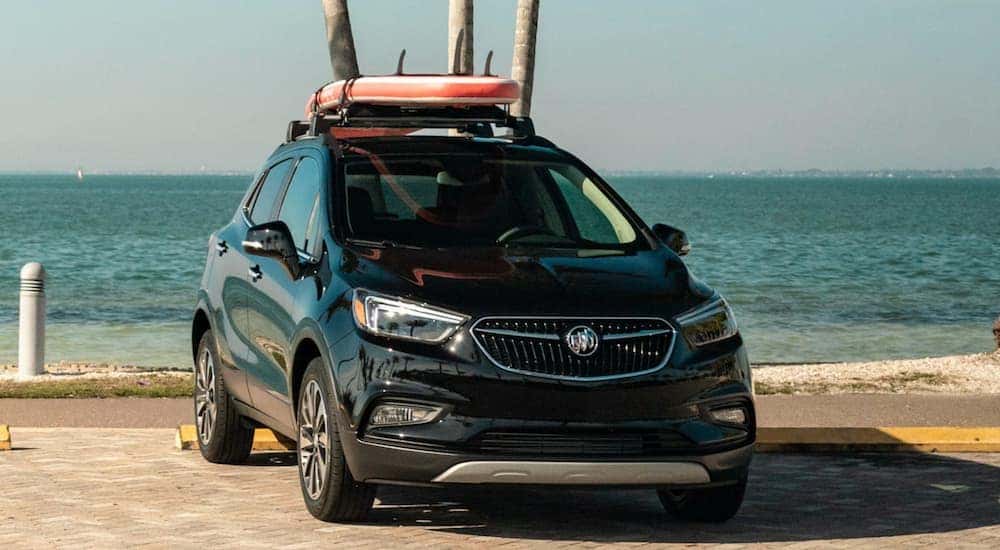 A black 2020 Buick Encore is parked next to a beach with a surf board the roof.