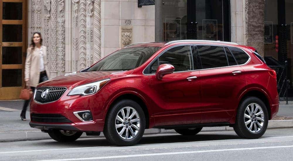 A smiling woman is walking to her red 2020 Buick Envision that's parked in front of a luxury hotel.